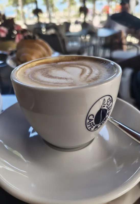 A cappuccino with latte art at a table by the promenade