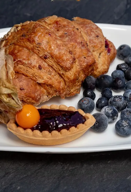 A wholegrain croissant with a blueberry tart and fresh blueberries