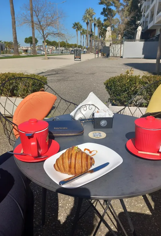 A croissant and two red cups on a terrace table by the promenade