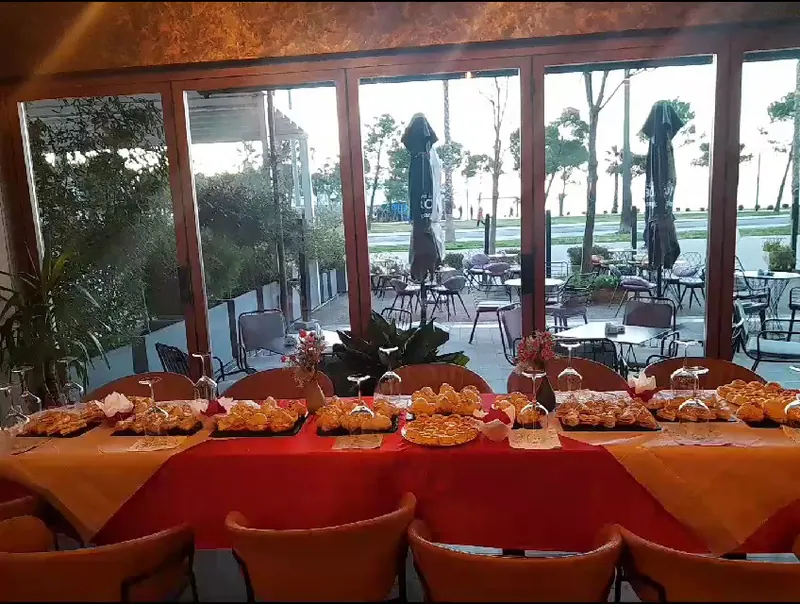 A long table of pastries in front of the windows facing the sea